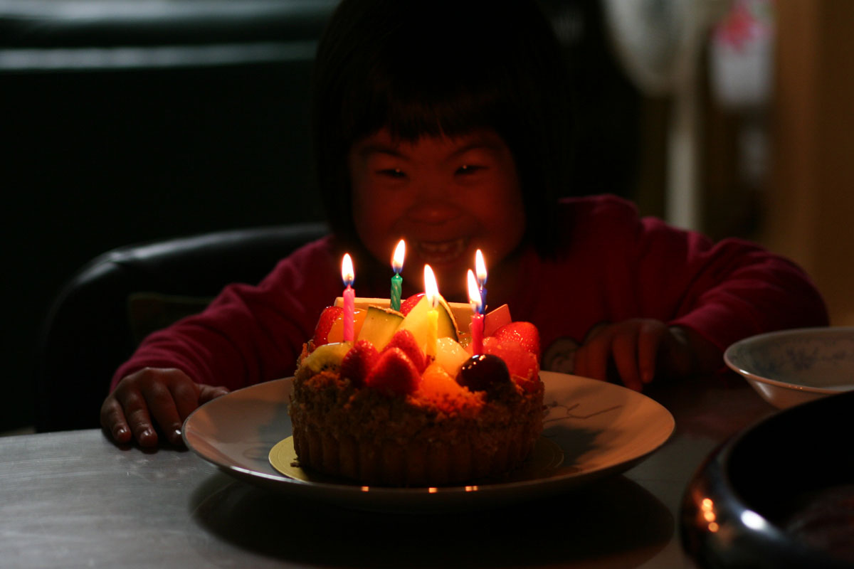５歳の誕生日ケーキのろうそくの火を消すダウン症の娘